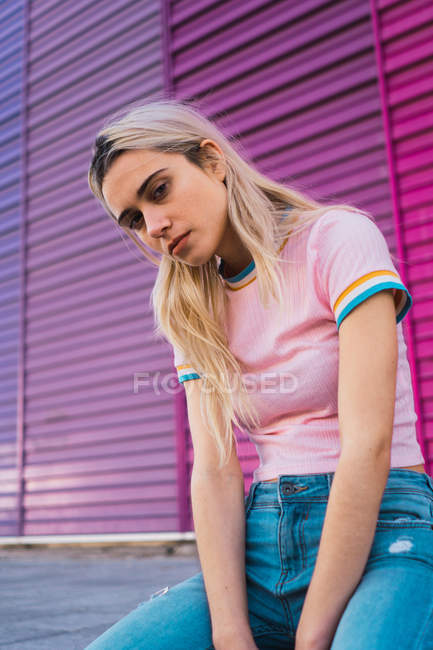 Mulher loira posando sentado contra parede multicolorida e olhando para a câmera — Fotografia de Stock