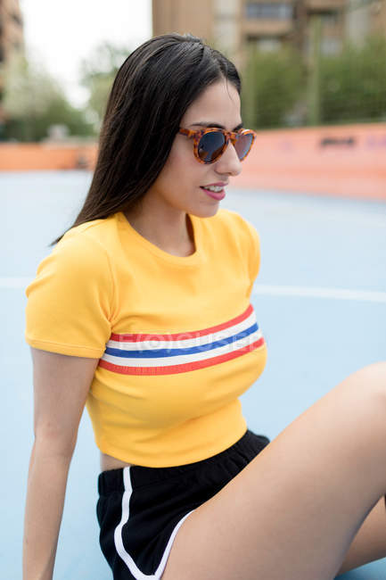 Jeune femme en lunettes de soleil assis sur le terrain de sport — Photo de stock