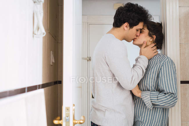 Jovem casal de pijama de pé e beijando na porta em casa — Fotografia de Stock