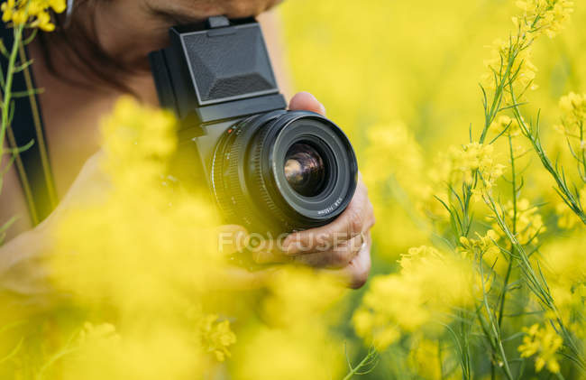 Primo piano della donna con fotocamera retrò scattare foto in natura con fiori gialli — Foto stock