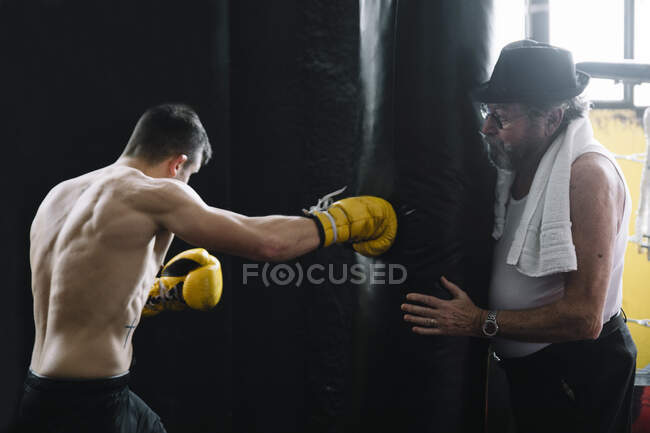 Взрослый тренер, стоящий и держащий в руках боксерскую грушу для спортсмена в спортзале. — стоковое фото