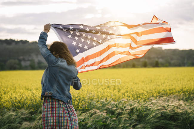 Женщина в цветной юбке с американским флагом в поле с желтыми цветами в День Независимости — стоковое фото