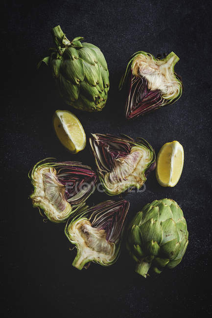 Fresh halved artichokes and pieces of lemon on black background — Stock Photo