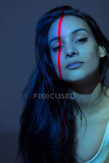Giovane donna attraente con linea rossa sul viso in piedi su sfondo grigio — Foto stock
