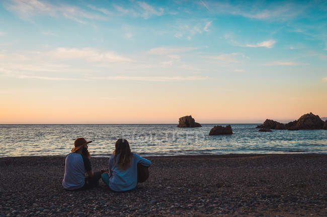 Uomo e donna seduti con la chitarra sulla spiaggia al mare — Foto stock