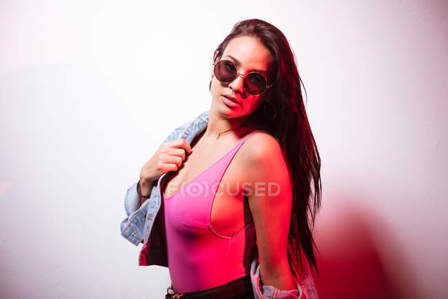 Pretty young pink dressed woman in sunglasses standing at white wall — Stock Photo