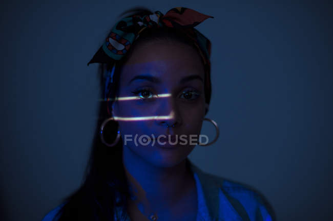 Jolie femme debout dans une pièce sombre avec deux petites lignes lumineuses sur le visage — Photo de stock
