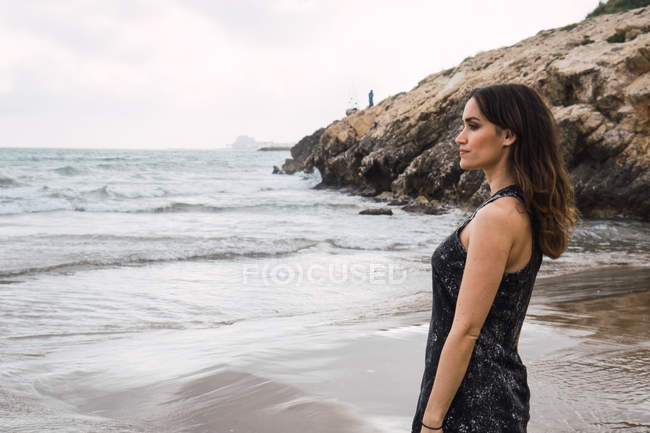 Elegante, nachdenkliche Frau, die am Strand steht und die Aussicht betrachtet — Stockfoto