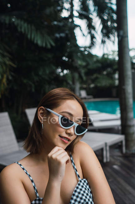 Retrato de jovem mulher em óculos de sol elegantes na piscina — Fotografia de Stock