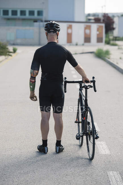 Back view of anonymous man with artificial arm standing on asphalt road near bicycle while having ride through city — Stock Photo
