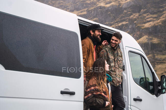 Group of cheerful men and woman in outwear standing in doors of traveling van in valley of Iceland. — Stock Photo
