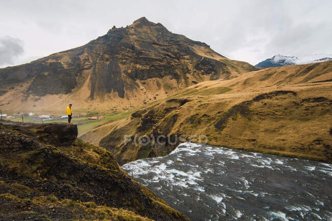 View of tourist standing on rock above flowing water with picturesque mountains on background, Iceland. — Stock Photo