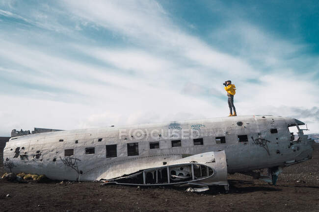 Side view of man with photo camera standing on top of crashed aircraft on ground of terrain in Iceland. — Stock Photo