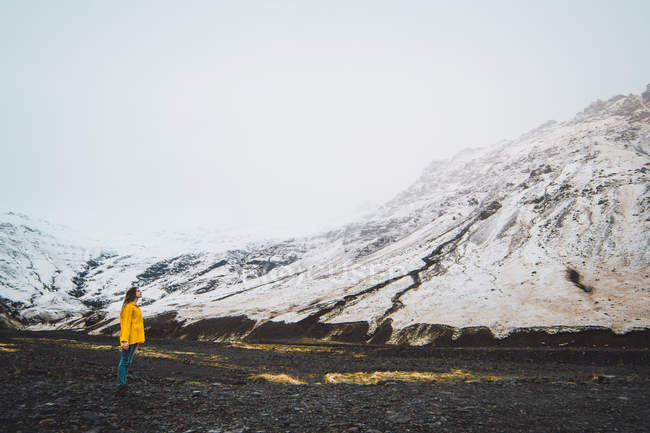 Жінка в жовтій куртці, що стоїть біля засніжених гір — стокове фото