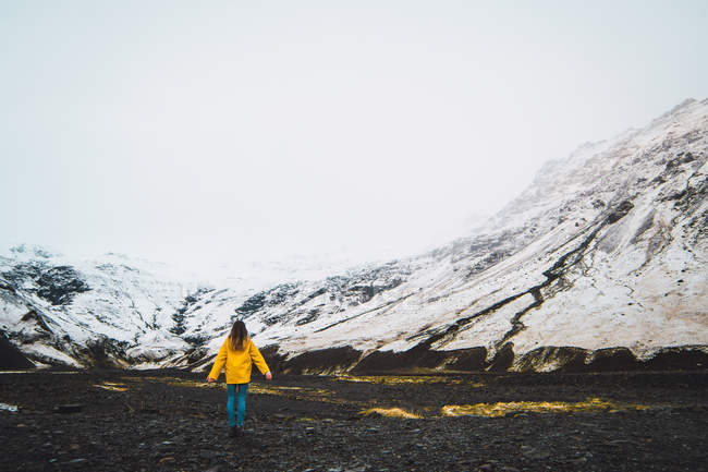 Жінка в жовтій куртці, що стоїть біля засніжених гір — стокове фото