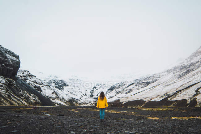Mujer de chaqueta amarilla parada cerca de montañas nevadas - foto de stock