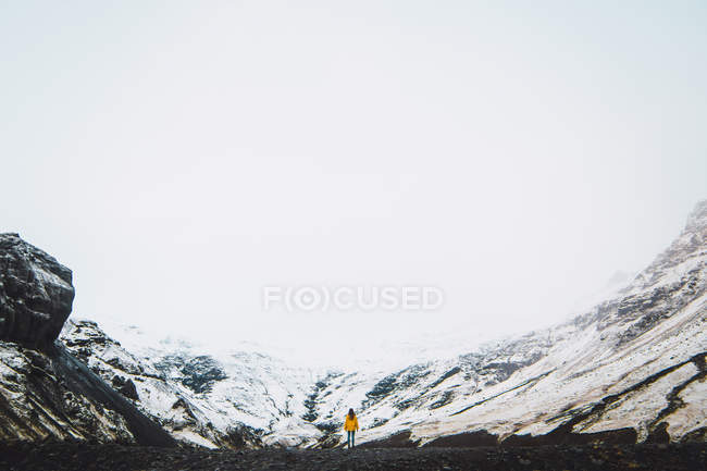 Woman in yellow jacket standing near snowy mountains — Stock Photo