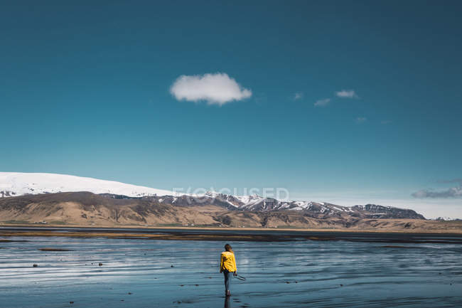 Donna in giacca gialla in piedi di fronte alle montagne con cielo limpido e guardando la vista — Foto stock