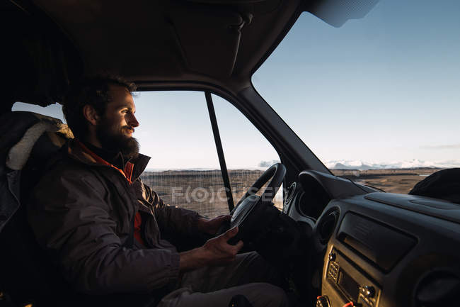 Homem barbudo sorridente dirigindo carro na estrada na natureza — Fotografia de Stock