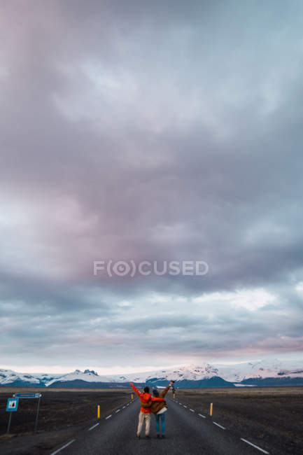 Embracing couple standing on road near mountains under dramatic sky — Stock Photo