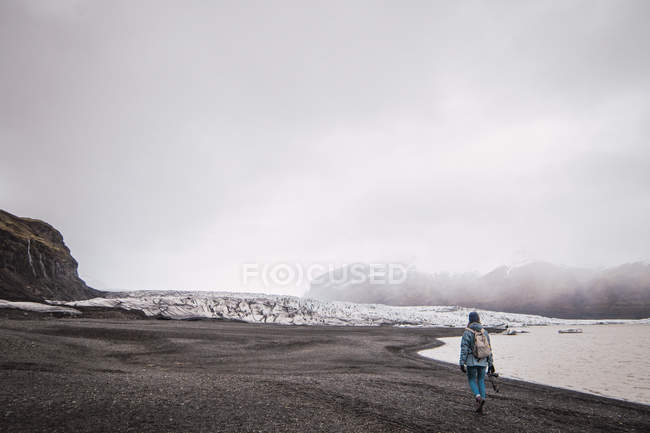 Mujer caminando por la costa con montañas nevadas en el fondo - foto de stock