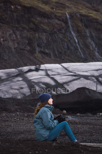 Frau sitzt an kalter Küste mit schwarzem Sand — Stockfoto
