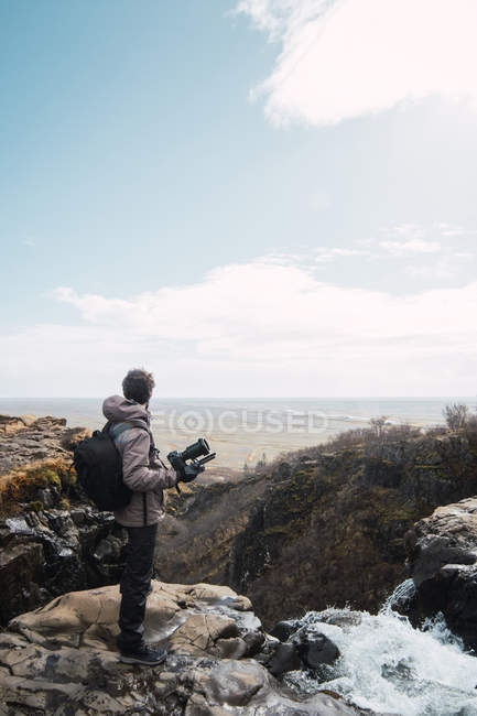 Fotógrafo masculino con mochila y cámara disfrutando de vista al mar desde la montaña - foto de stock