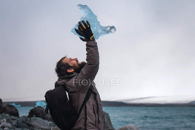 Man sitting on coast with piece of ice above head — Stock Photo