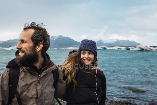 Bearded man and laughing woman in warm clothes standing on background of cold sea in Iceland — Stock Photo