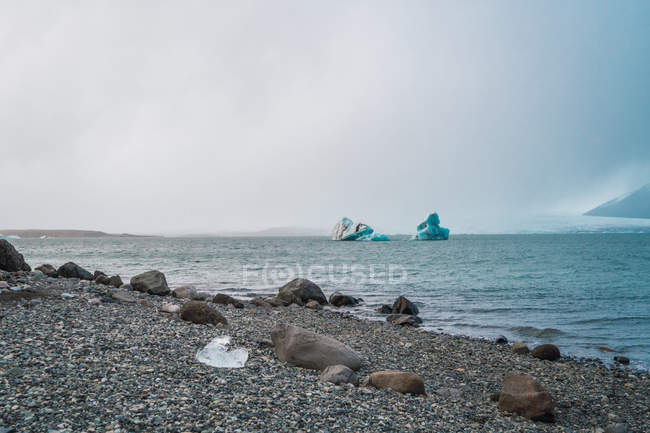 Morceaux de glace dans l'eau et la plage avec cailloux et rochers, Skaftafell, Vatnajokull, Islande — Photo de stock