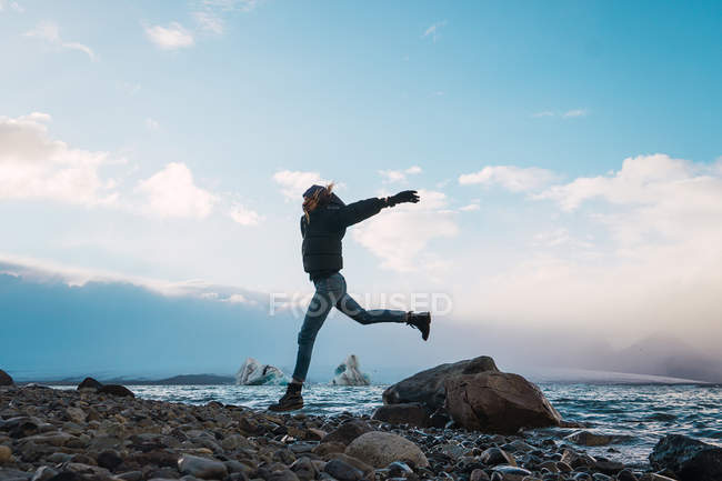 Happy girl jumping on rocks at cold sea — Stock Photo