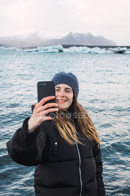 Усміхнена молода жінка бере селфі на холодному пляжі — стокове фото