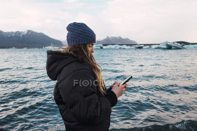 Femme utilisant un smartphone sur la plage froide — Photo de stock