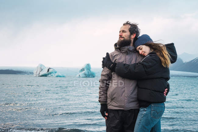 Amar abrazar pareja de pie en el frío paisaje marino - foto de stock