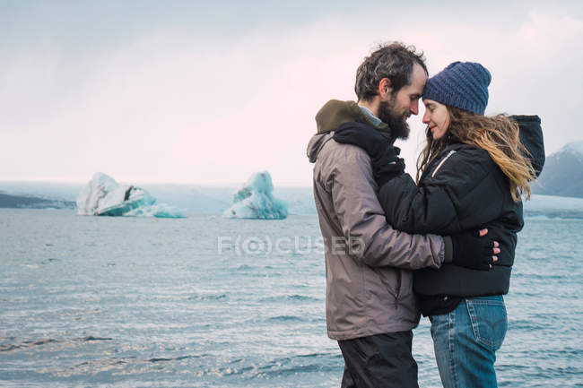 Casal feliz abraçando com cabeça a cabeça na costa do mar islandês — Fotografia de Stock