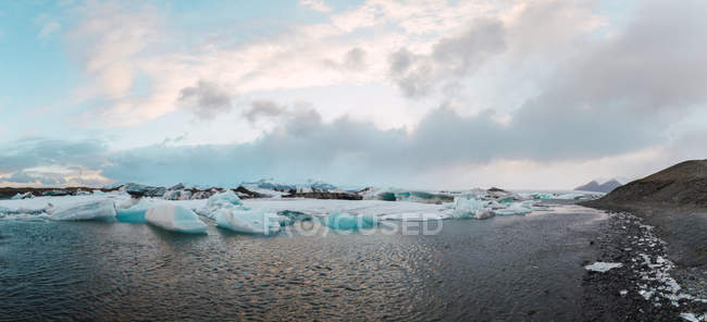 Пейзаж берегової лінії з фрагментами льодовика Jokulsarlon на тлі скелястих гір на заході сонця — стокове фото