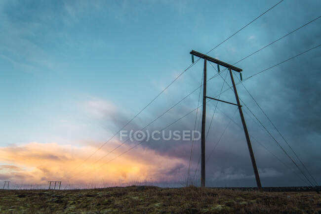 Vista de postes eléctricos con cables en la tranquila llanura bajo el crepúsculo cielo azul con nubes, Islandia. - foto de stock