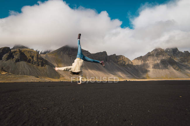 Женщина делает стойку на руках с одной стороны с горами на заднем плане, Исландия — стоковое фото