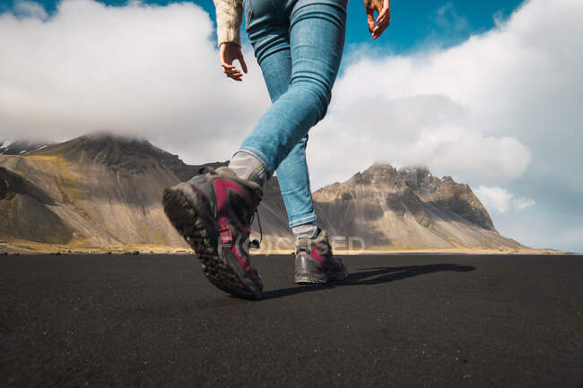 Faceless shot from below of woman in trekking shoes walking on valley ground with mountains on background, Iceland. — Stock Photo