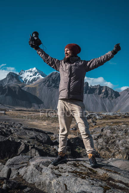 Веселый фотограф, стоящий на скале с горами на заднем плане, Исландия — стоковое фото