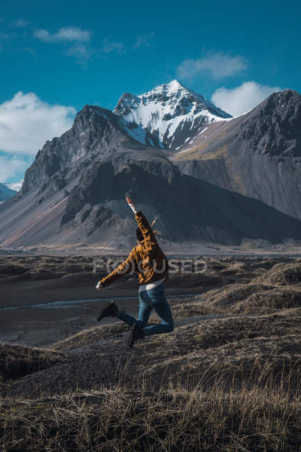 Женщина прыгает высоко над землей в долине с скалистыми горами, Исландия — стоковое фото
