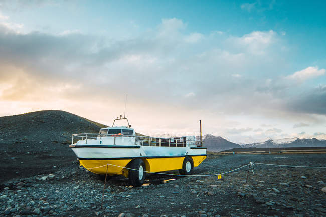 Бело-желтая лодка с колесами, стоящая на каменистом холме, Скафтафелл, Ватнайокудль, Исландия — стоковое фото