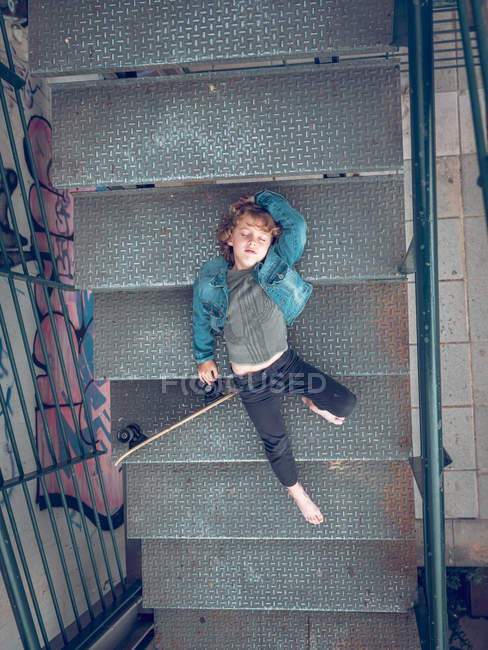 Menino deitado com skate nas escadas — Fotografia de Stock