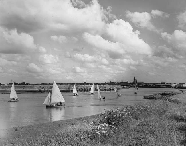 Foto en blanco y negro de veleros flotando en el agua del río bajo el cielo nublado . - foto de stock