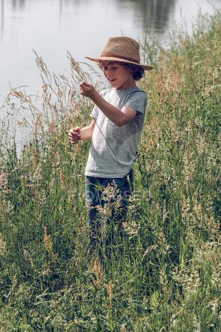 Garçon debout dans l'herbe au lac — Photo de stock