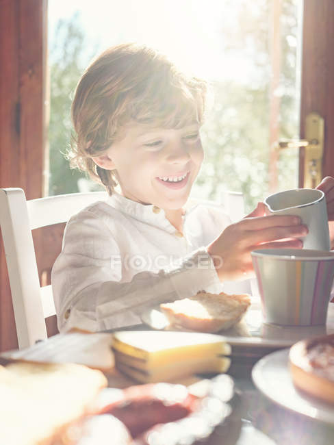 Little boy with cup sitting at table — Stock Photo