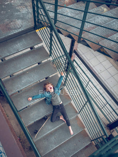 Niño acostado con monopatín en las escaleras - foto de stock