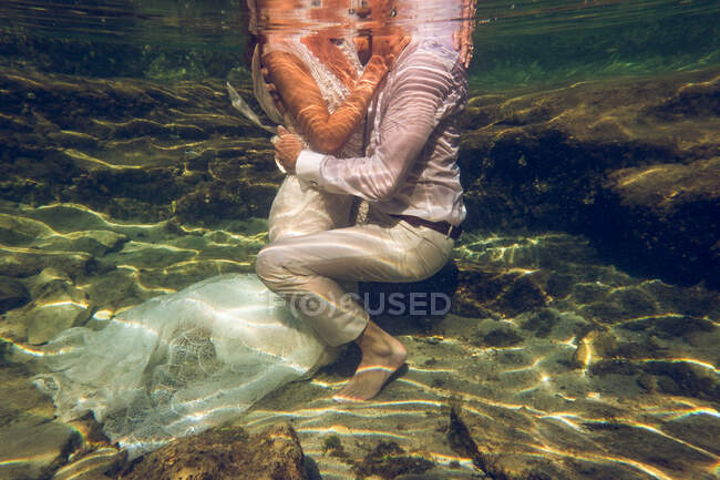 Casal irreconhecível em trajes de casamento sentado no fundo do mar e abraçando uns aos outros. — Fotografia de Stock