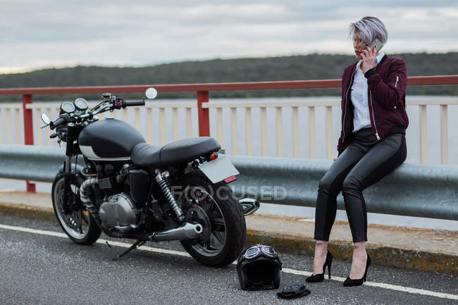 Жінка говорить на смартфоні поруч з мотоциклом — стокове фото