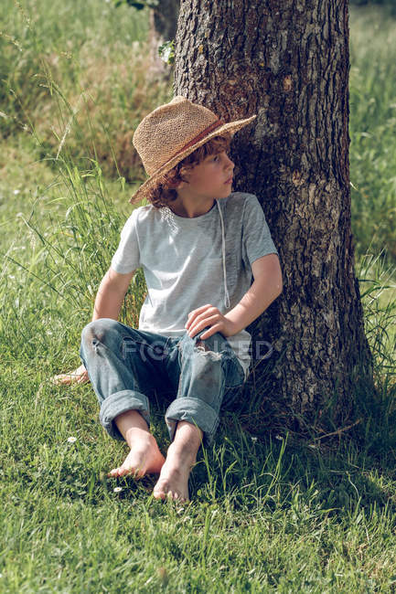 Descalzo niño sentado bajo el árbol - foto de stock